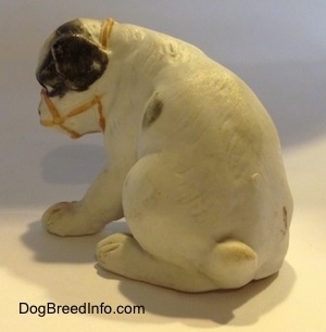 The back of a white with black bone china Bulldog puppy figurine that has a muzzle on it. The figurine has a small tail.