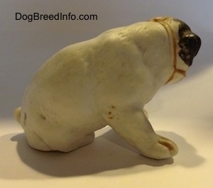The right side of a white with black bone china Bulldog puppy figurine that has a muzzle on it. The figurine has fine paw details.