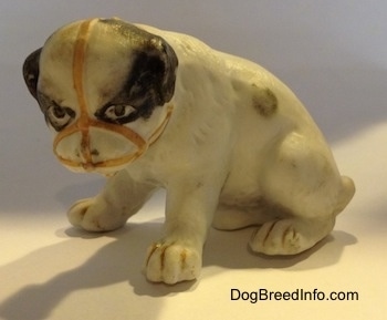The left side of a white with black bone china Bulldog puppy figurine that has a muzzle on it. The figurine has black circles for eyes.
