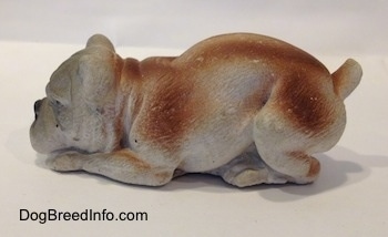 The left side of a cement mold paperweight made that is a brown with white English Bulldog figurine that is laying down. The figurine has fine hair details.