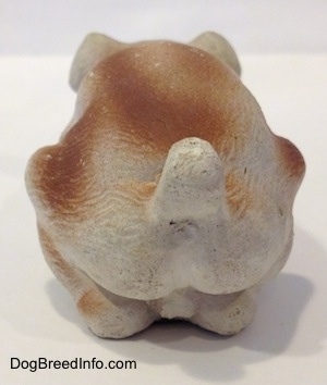 The back of a cement mold paperweight made that is a brown with white English Bulldog figurine that is laying down. The figurine has its short tail arched up.