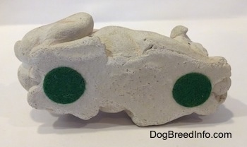 The underside of a cement mold paperweight made that is a brown with white English Bulldog figurine that is laying down. There are two green stickers at the bottom of the figurine.