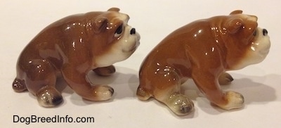 The right side of two brown with white miniature Bulldogs that are in a sitting pose. The figurines have black circles for eyes and they are cartoony.