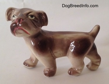 The left side of a brown and white ceramic Bulldog figurine. The figurine has pink lines around its nose and mouth.