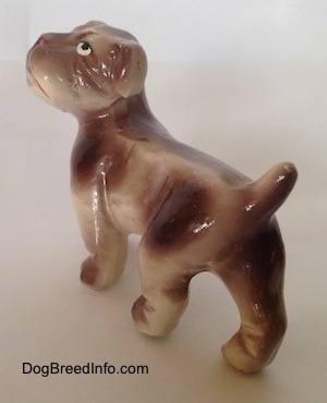 The back left side of a brown and white ceramic Bulldog figurine. The figurines tail is arched up.