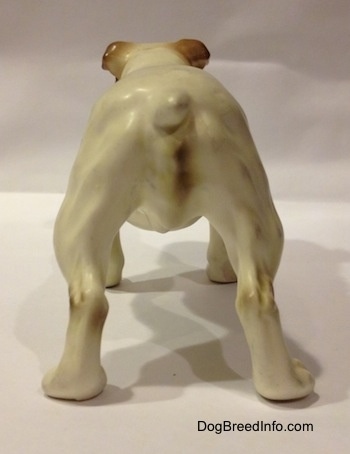 The back of a porcelain white with brown Bulldog figurine. It is hard to differentiate the tail of the figurine from the body.