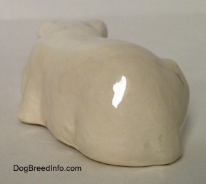 The back of a miniature white English Bulldog figurine that is in a lying down pose with a brown spot over its left eye. The tail of the figurine is hard to differentiate from the body.