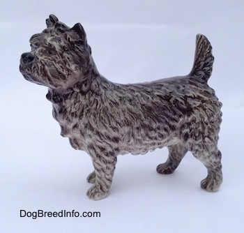 The left side of a gray and white Cairn Terrier. The tail of the figurine is arched up.