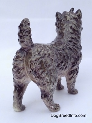 The back right side of a gray and white Cairn Terrier figurine. The figurines tail is arched up.