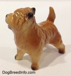 The front left side of a brown with black Cairn Terrier figurine. The paws of the figurine are black.