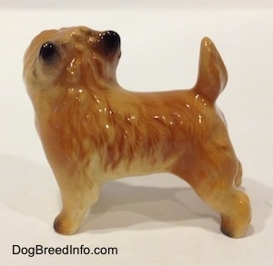 The left side of a brown with black Cairn Terrier figurine. The figurine has fine hair details, a tail that is up in the air and small black perk ears. Its body is tan.
