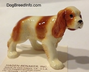 The front right side of a red and white Cavalier King Charles Spaniel figurine. The figurine has black circles for eyes.