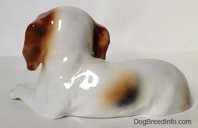 The left side of a white with brown and black Cavalier King Charles Spaniel figurine that is laying down.