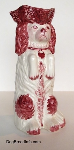 The front right side of a white and red Cavalier King Charles Spaniel porcelain water pitcher. The pitcher has a red collar on it.