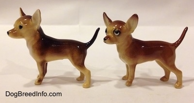 The left side of two Chihuahua ceramic figurines that look different. The left most figurine has black circles for eyes.