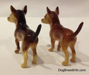 The back right side of two different ceramic Chihuahua figurines. The figurines have large ears and long tails.