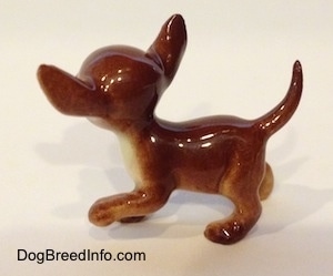 The left side of a brown with tan ceramic Chihuahua dog figurine. The figurine has a round head.