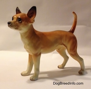 The left side of a porcelain tan with white Chihuahua figurine. The figurine has detailed eyes and a whisker dots around its muzzle.