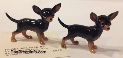 The right side of two different black with tan Chihuahua figurines. The figurines are glossy.