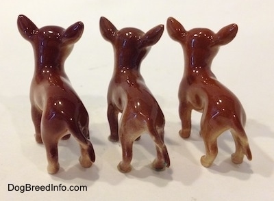 The back of three different ceramic Chihuahua figurines. The figurines have long tails.