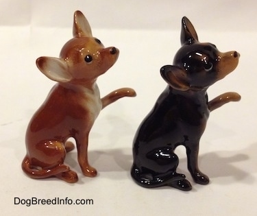 The right side of two different looking Chihuahua figurines that have one paw in the air. The figurines have long tails.