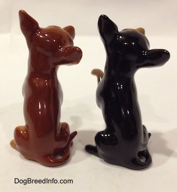 The back of two different Chihuahua figurines that have a paw in the air.