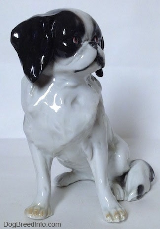 The front of a white with black Japanese Chin dog figurine. The figurine has yellow nails at the top of its paws.