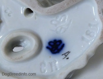 Close up - The underside of a Japanese Chin dog figurine. There is a stamp and an engraving of the Goebel Double crown mark logo.