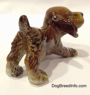 The back right side of a brown and tan Cocker Spaniel puppy figurine. The figurine has detailed hair brushings.