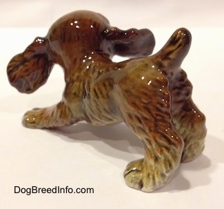 The back left side of a brown and tan Cocker Spaniel puppy figurine. The figurine has very detailed hair.