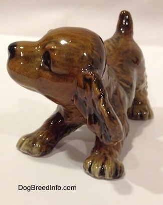 The front left side of a brown and tan Cocker Spaniel puppy figurine. The figurine is designed to look like it is bowing.