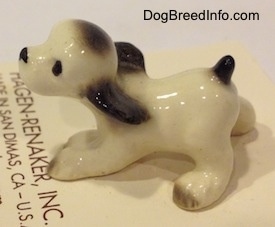 The left side of a white with black ceramic Cocker Spaniel puppy figurine. The figurine eyes are black circles.