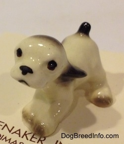 The front left side of a white with black ceramic Cocker Spaniel puppy figurine. The figurine has light face details.