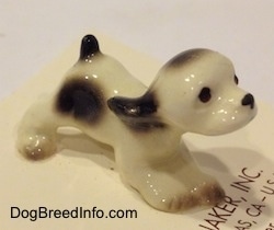 The front right side of a white with black ceramic Cocker Spaniel puppy figurine. It has light details.