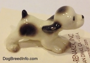 The right side of a white with black ceramic Cocker Spaniel puppy figurine. The front paws of the figurine are connected together.