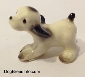 The left side of a white with black ceramic Cocker Spaniel puppy figurine.