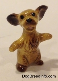A tan with brown Cocker Spaniel figurine is sitting on its hind legs, it has its paws and ears out.