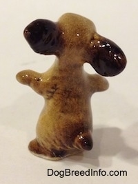 The back of a tan with brown Cocker Spaniel figurine is sitting on its hind legs, it has its paws and ears out. It has a small tail.