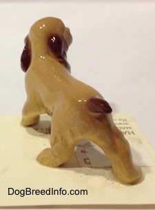 The back left side of a tan with brown ceramic Cocker Spaniel figurine. It is very glossy.