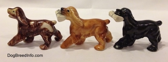 The left side of three different Cocker Spaniel figurines. Two out of three of the figurines have newspaper in there mouths.