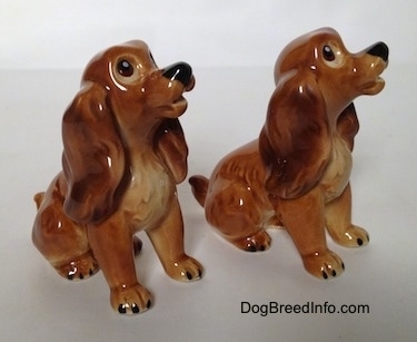 The front right side of two brown and tan Cocker Spaniel puppy figurines. The figurines have there mouths slightly open.