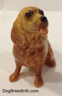 A tan ceramic Cocker Spaniel figurine that is sticking its tongue out. The figurine has fine hair details.