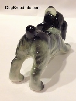 The back right side of a white and black Cocker Spaniel puppy figurine. Its tail is in the air.