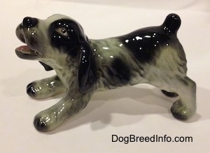 The left side of a white and black Cocker Spaniel puppy figurine. It has lightly detailed hair brushings.