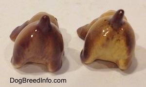 The back side of two brown and tan ceramic Cocker Spaniel puppy figurines that are play bowing. The back end of the dogs do not have hair brushings.