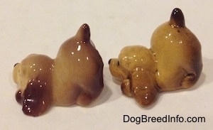 The left side of two brown and tan ceramic Cocker Spaniel puppy figurines that are play bowing. They have sort tails.