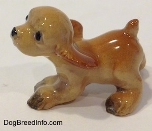 The left side of a tan ceramic Cocker Spaniel puppy running figurine. It is very glossy. The dog looks playful. The docked tail is short.