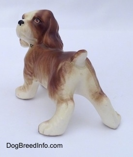 The back left side of a brown and white ceramic Cocker Spaniel puppy figurine. The figurine has a small tail.