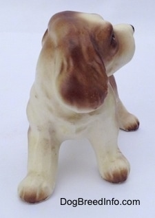 A brown and white ceramic Cocker Spaniel puppy figurine. The figurine is looking to the right and it has fine details on its ears.