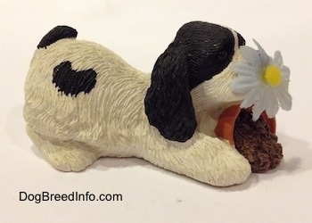 The right side of a sandicast black and white American Cocker Spaniel that is sniffing a flower out of a knocked over pot figurine.